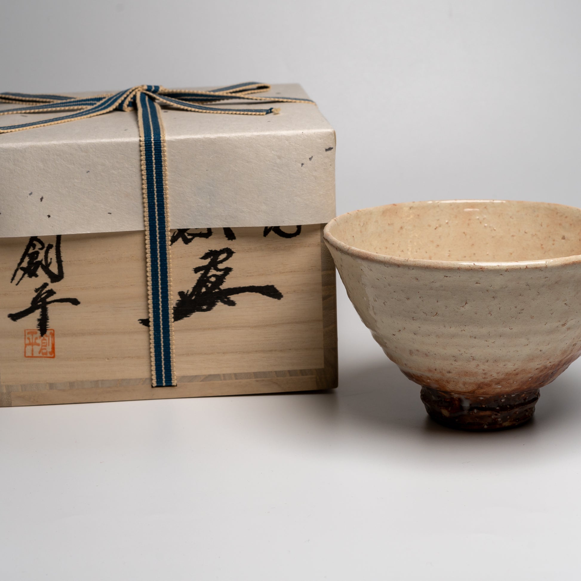 A Japanese ceramic ceremonial matcha tea bowl with its box on a white background
