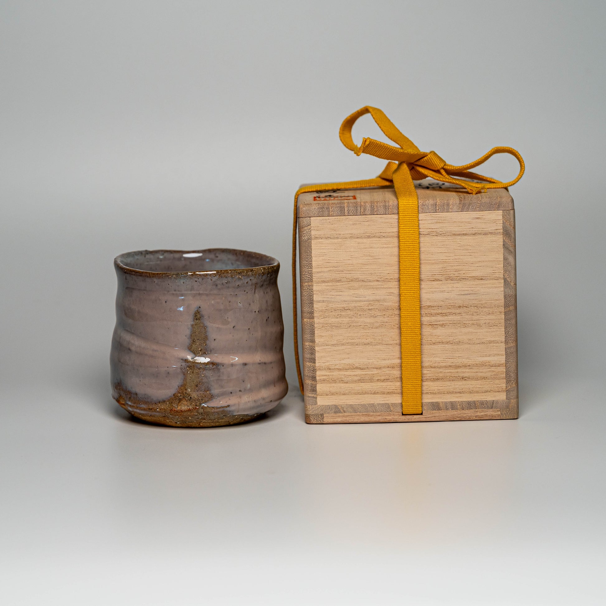 A pink Hagi yaki shochu cup next to its wooden box on a white background