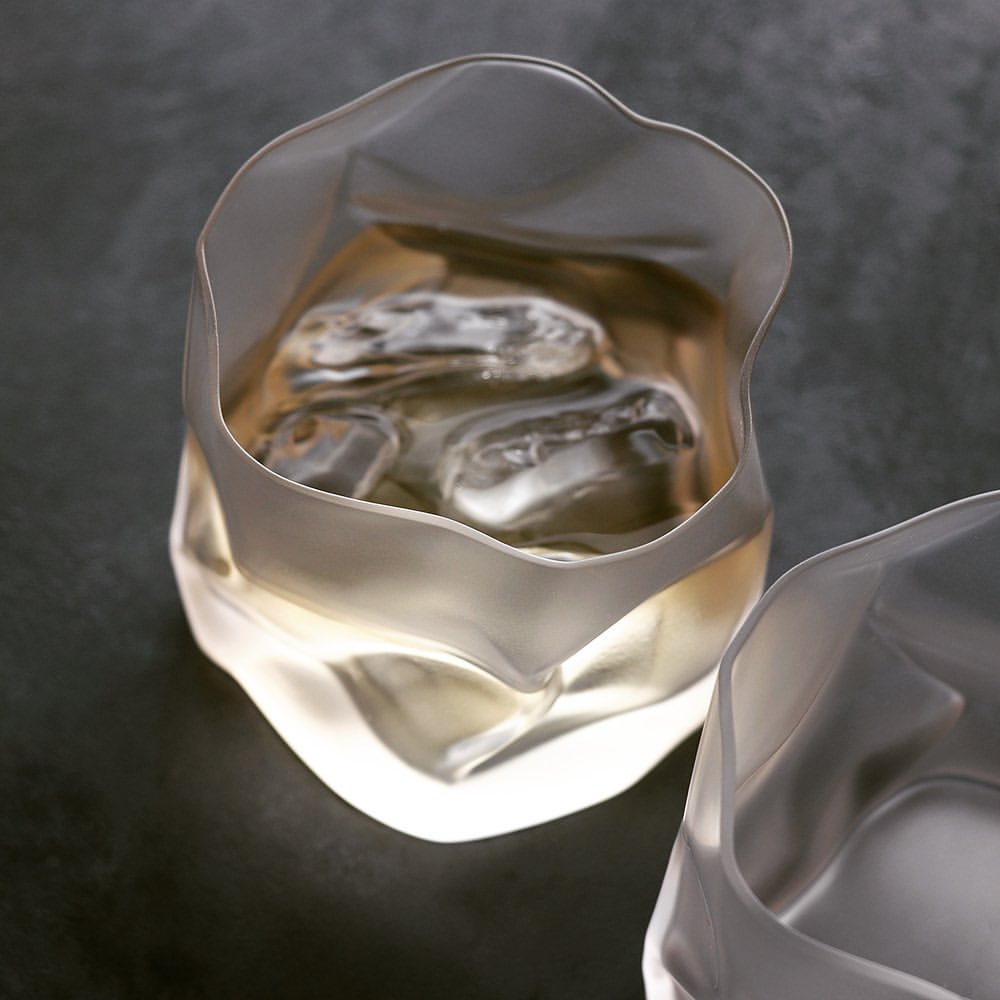 A filled frosted crumple whiskey glass on a table top