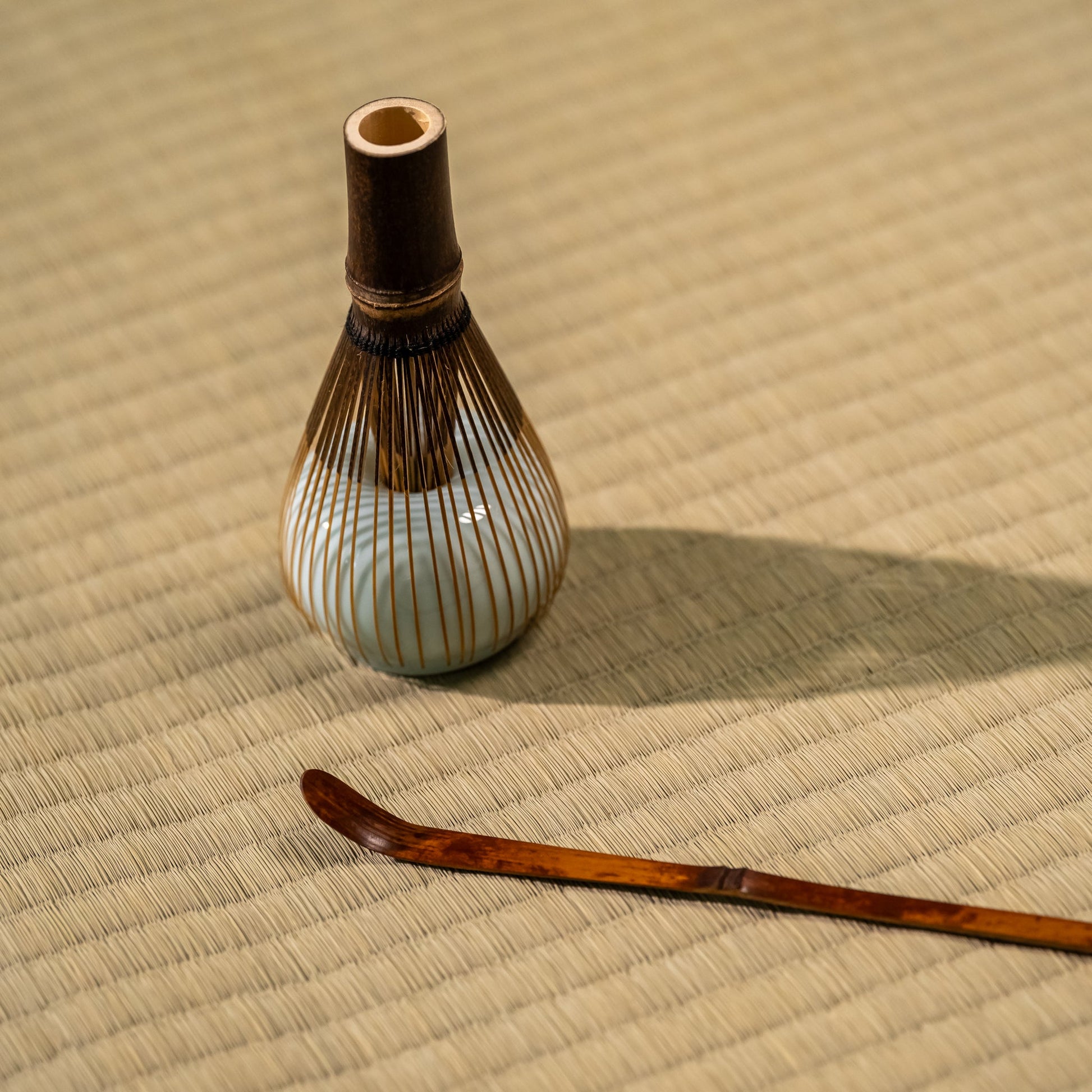 A Japanese matcha whisk and bamboo spoon on a tatami mat