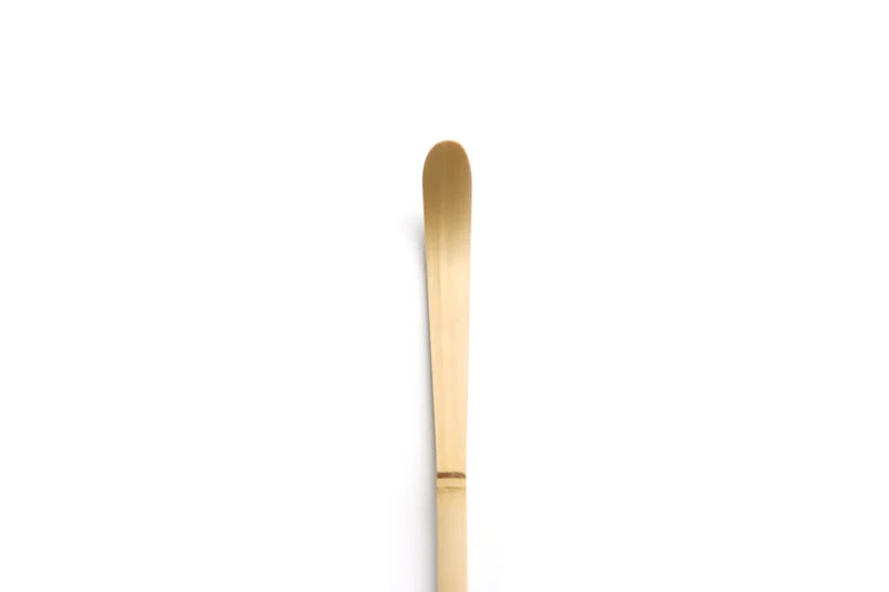 A close up of a white bamboo tea scoop on a white background