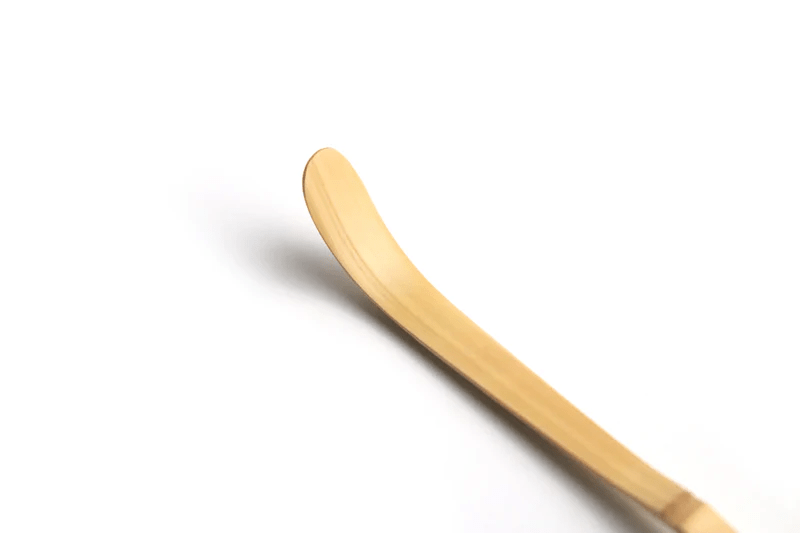 A close up of a white bamboo tea scoop on a white background