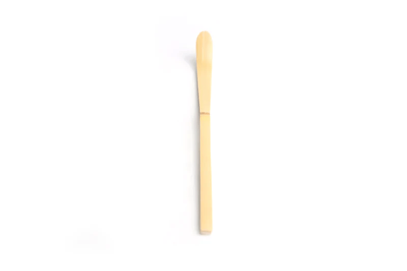 A close up of a white bamboo tea scoop on a white background