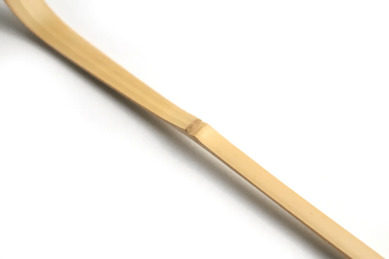 A close up of a white bamboo tea scoop on a white background