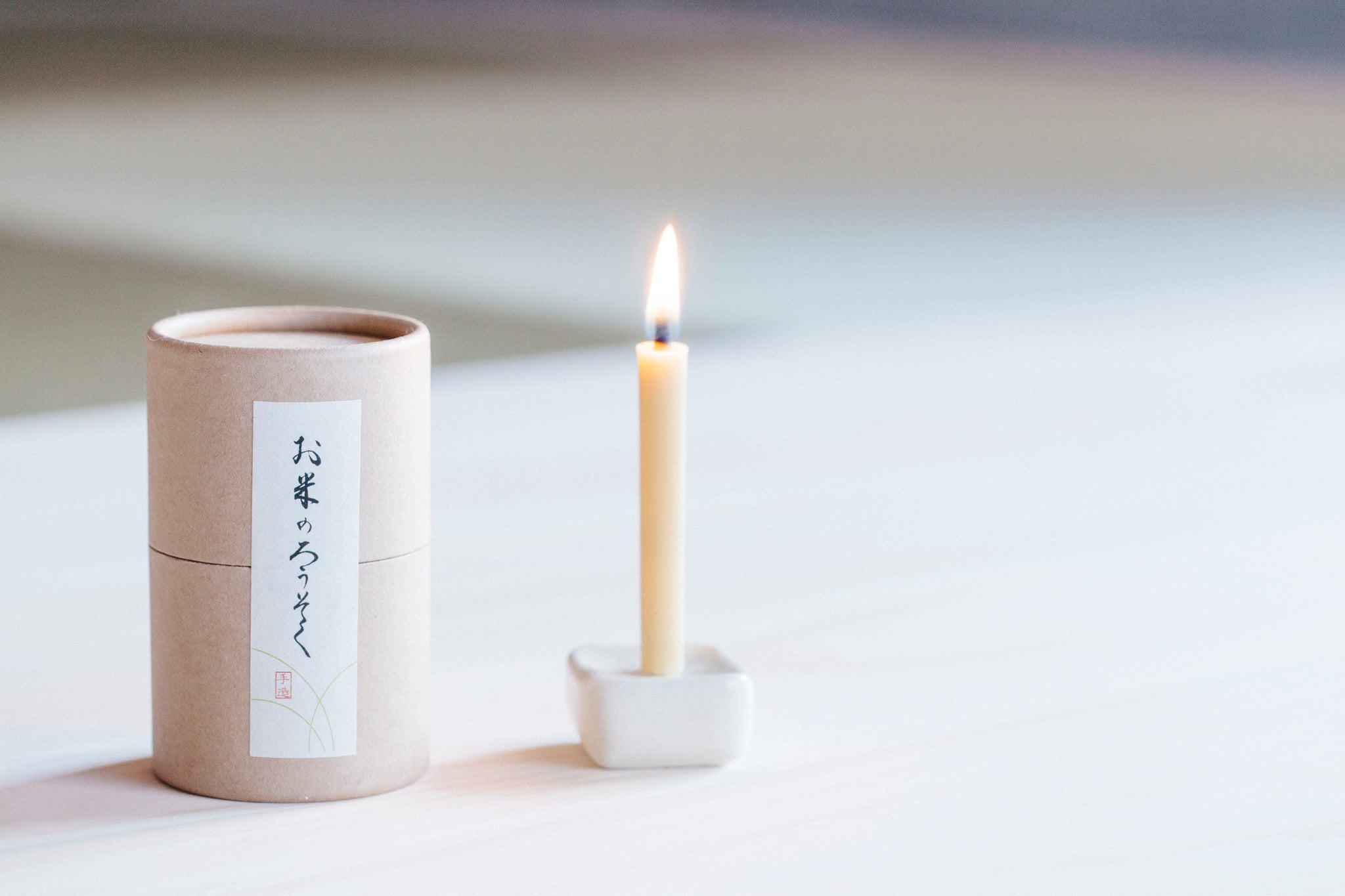 A lit rice wax candle next to a box of rice wax candles