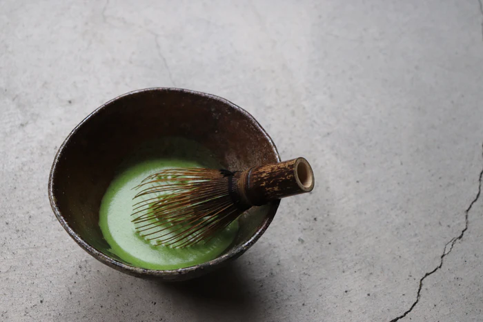 A black Takayama chasen matcha whisk in a bowl of matcha