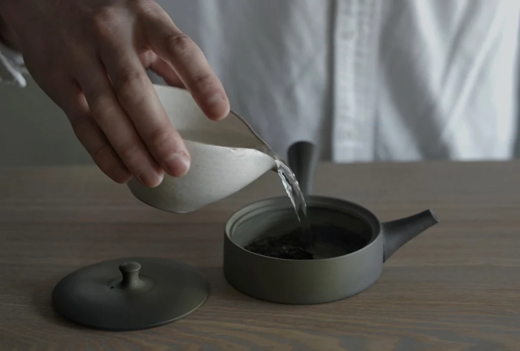 Pouring water into a Japanese ceramic teapot with Japanese green tea leaves