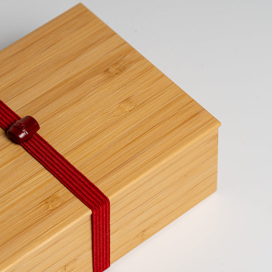 A close up of bamboo bento box with red strap on a white background