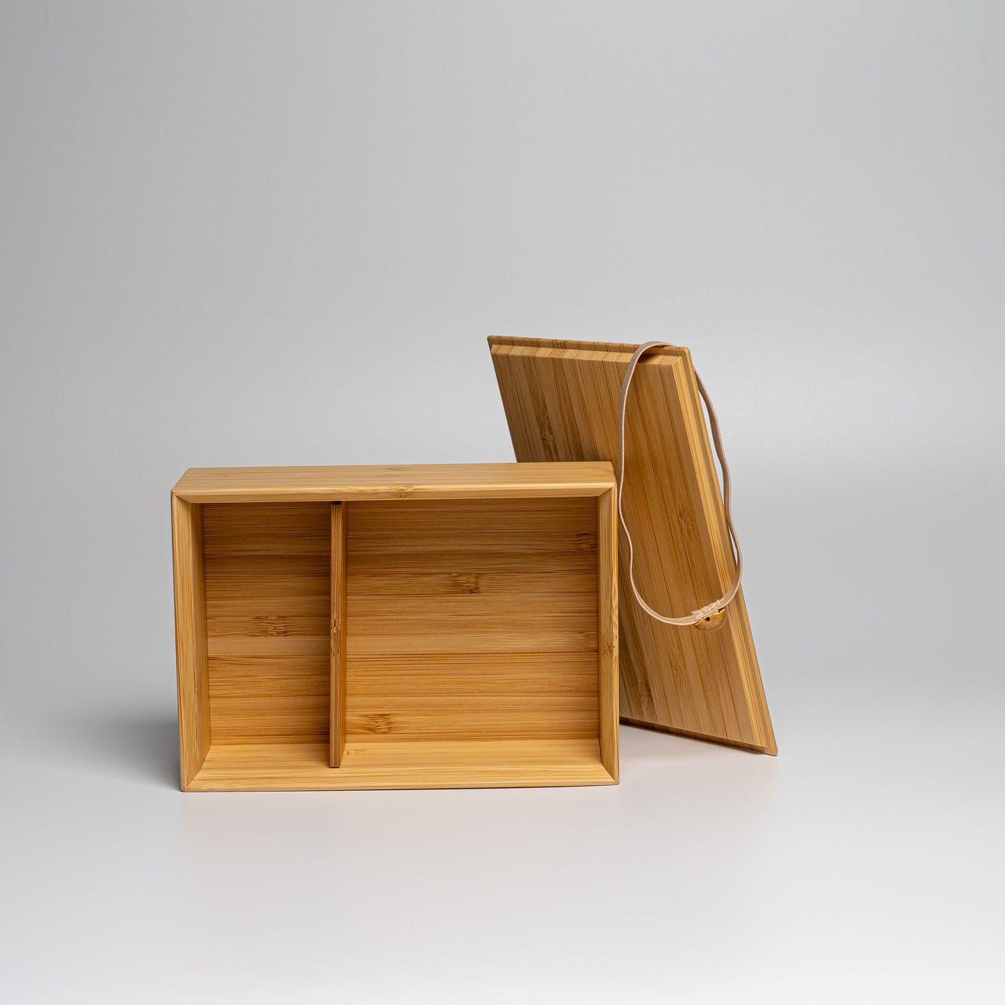 An open bamboo bento box with natural strap on a white background