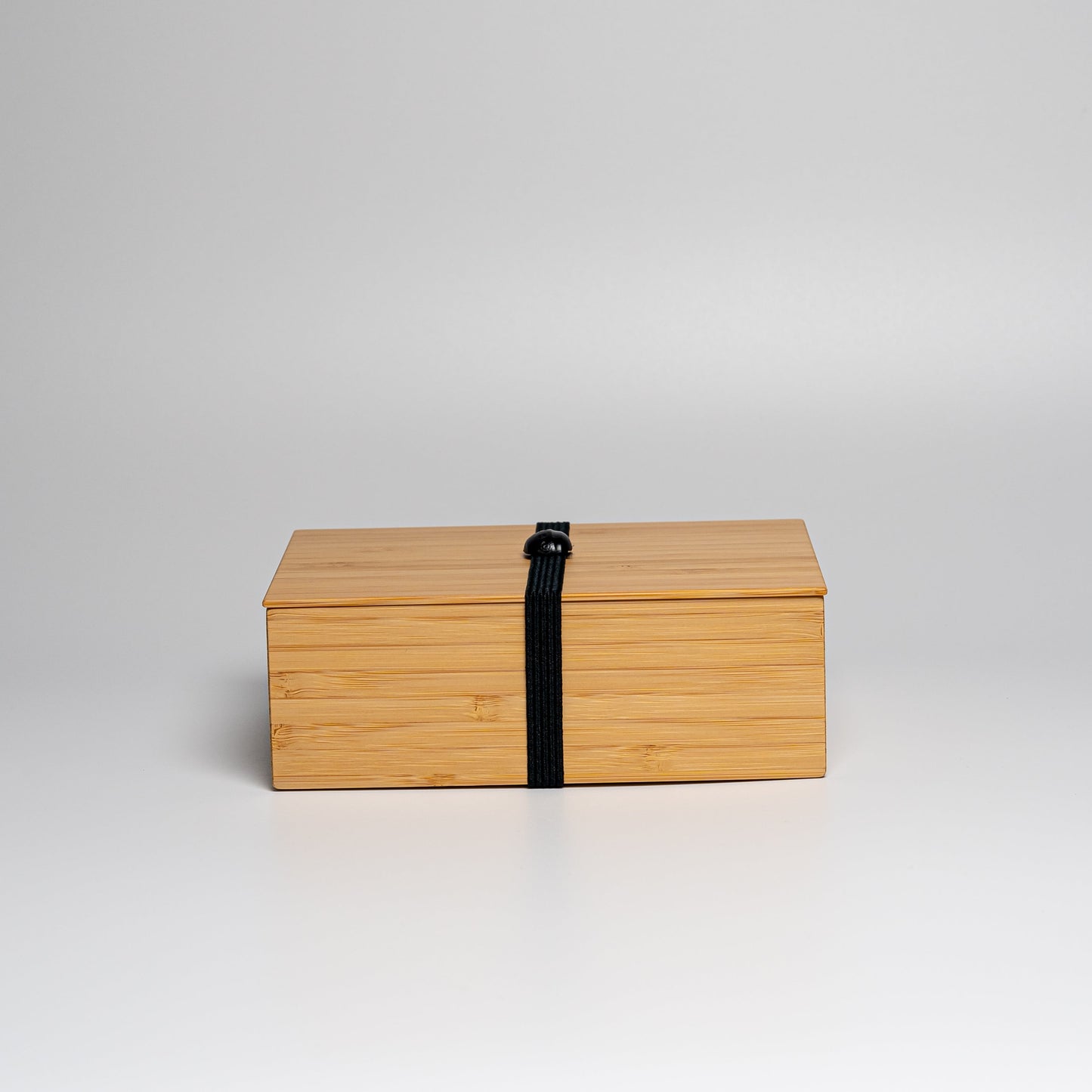 A bamboo bento box with black strap on a white background