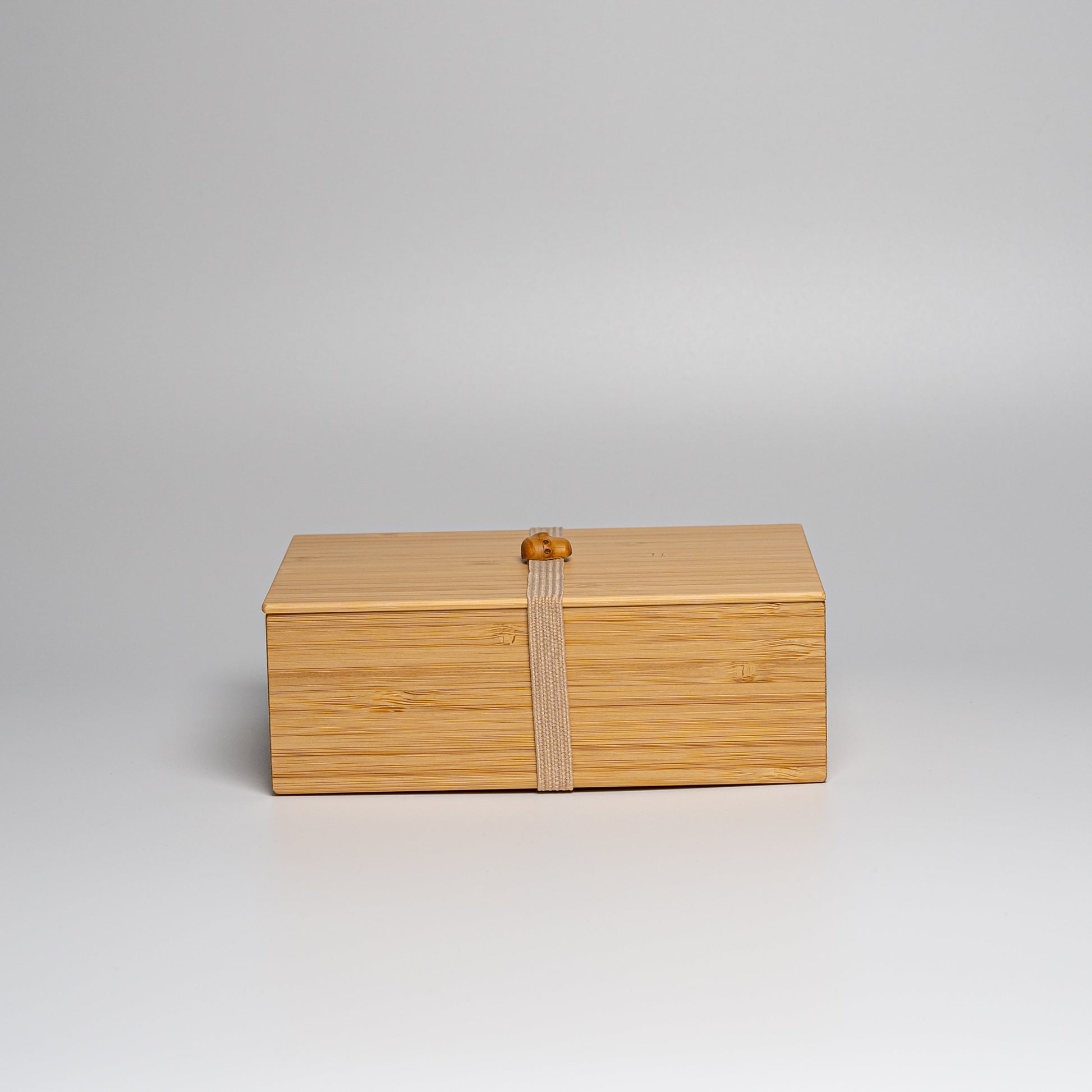 A bamboo bento box with natural strap on a white background