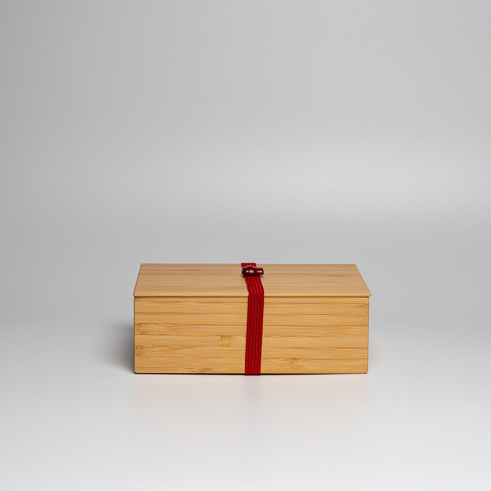 A bamboo bento box with red strap on a white background
