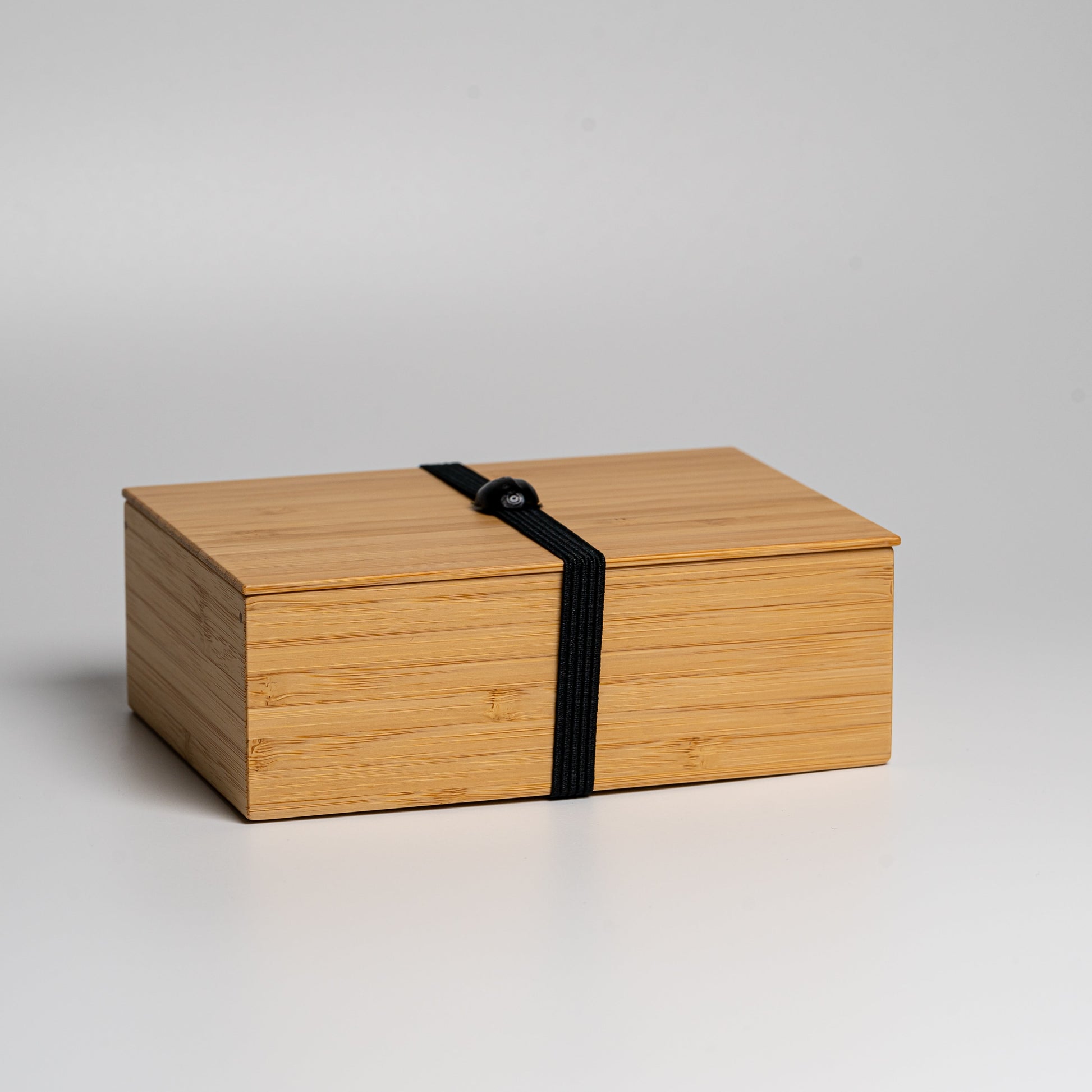 A bamboo bento box with black strap on a white background