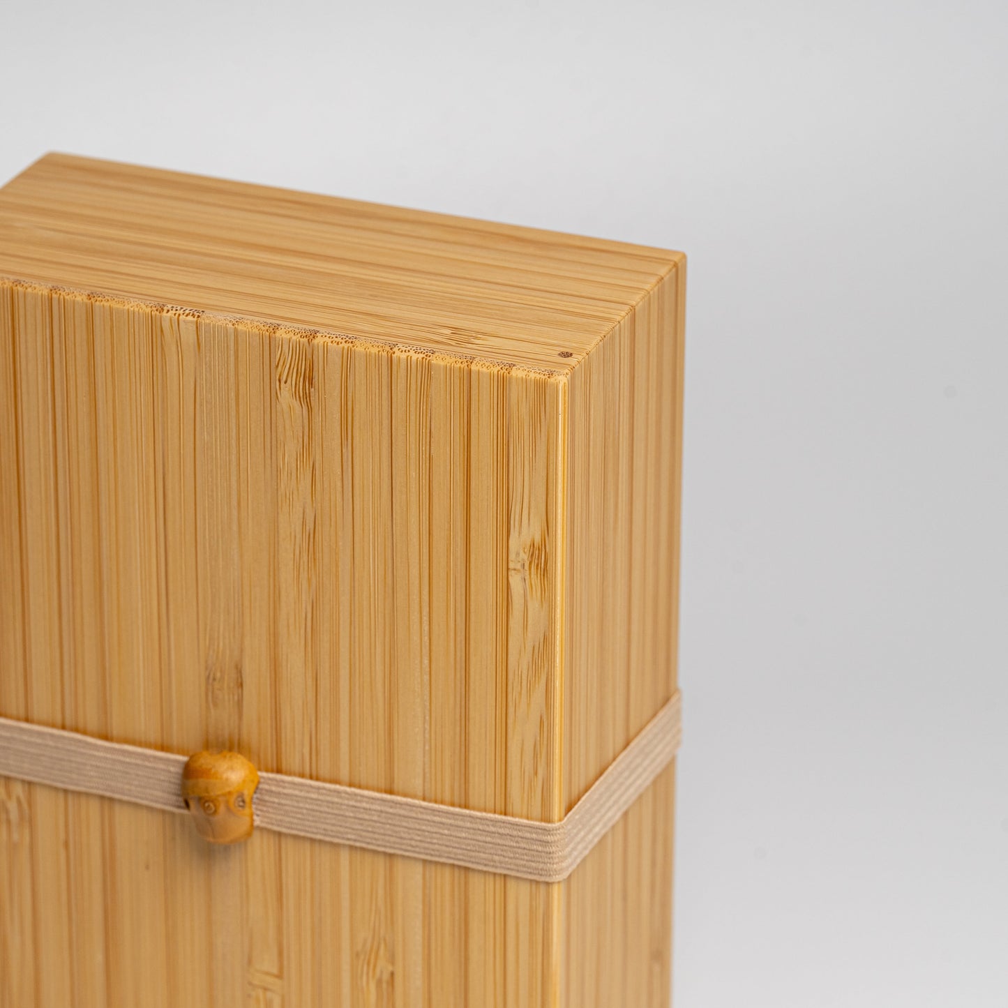A close up of a bamboo bento box with natural strap on a white background