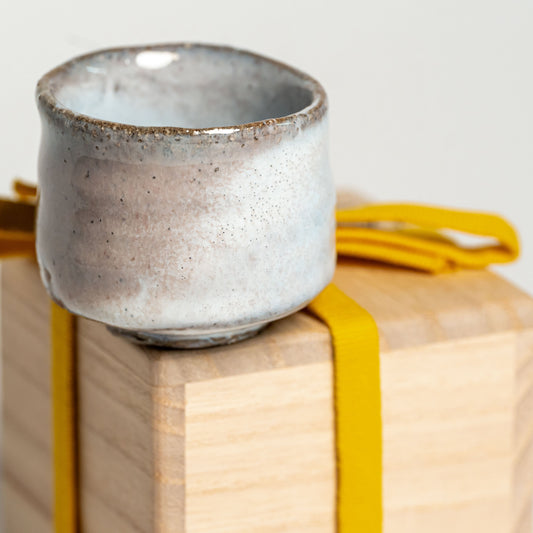 A pink and white Hagi yaki sake cup on its wooden box on a white background