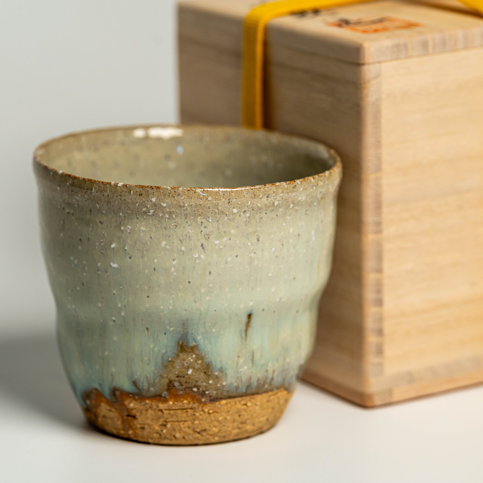 A close up of a green Hagi yaki shochu cup next to a wooden box