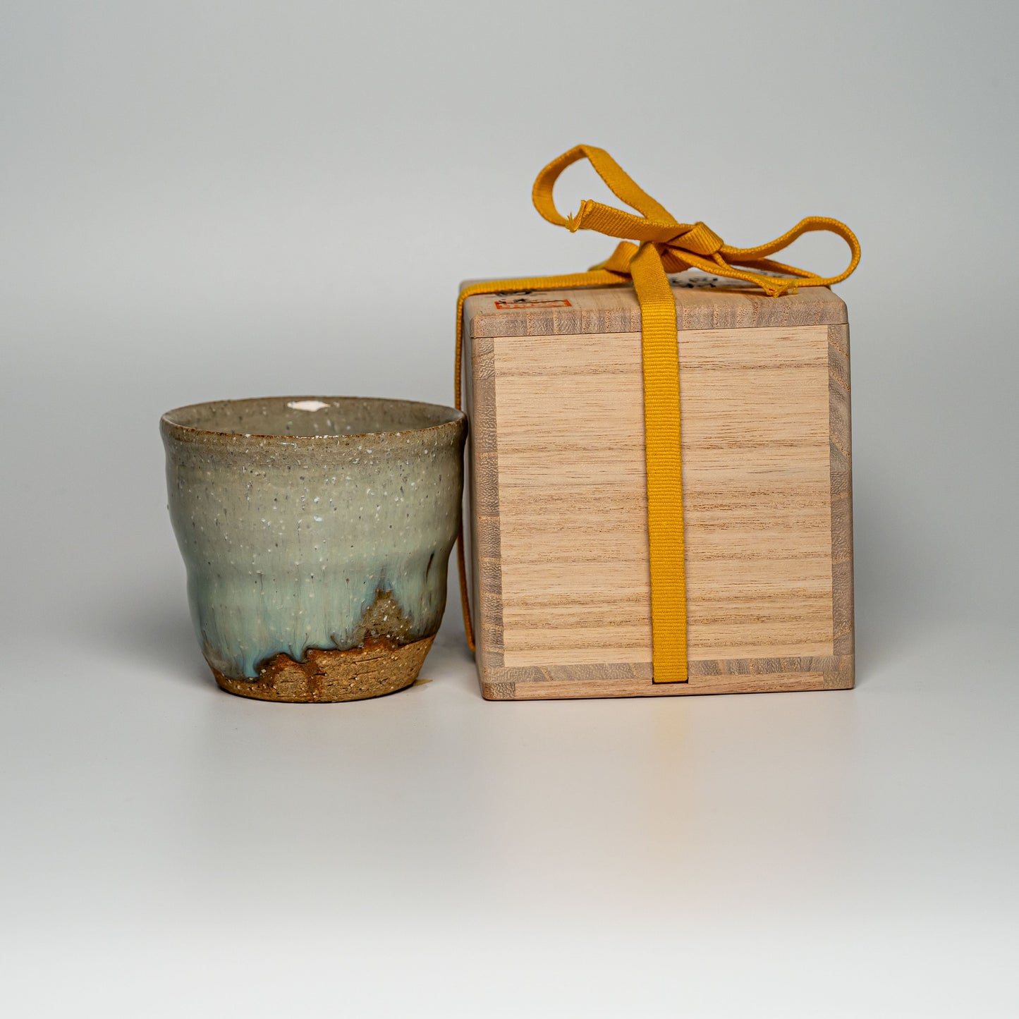 A green Hagi yaki shochu cup next to its wooden box on a white background