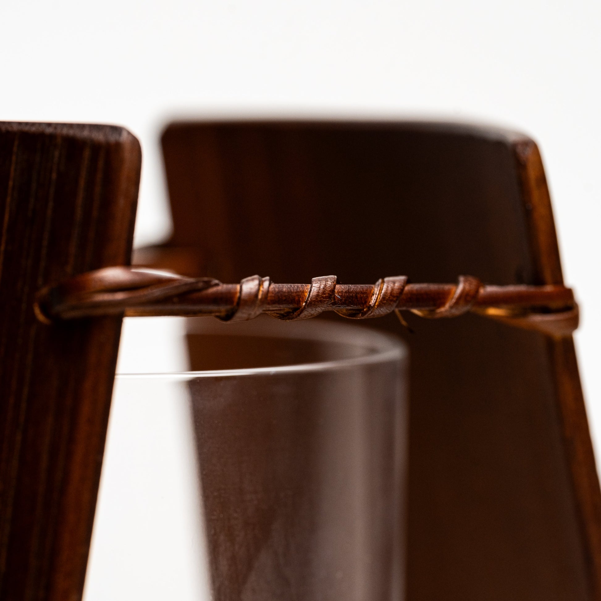 A close up of an empty brown bamboo Noshi flower vase on a white background