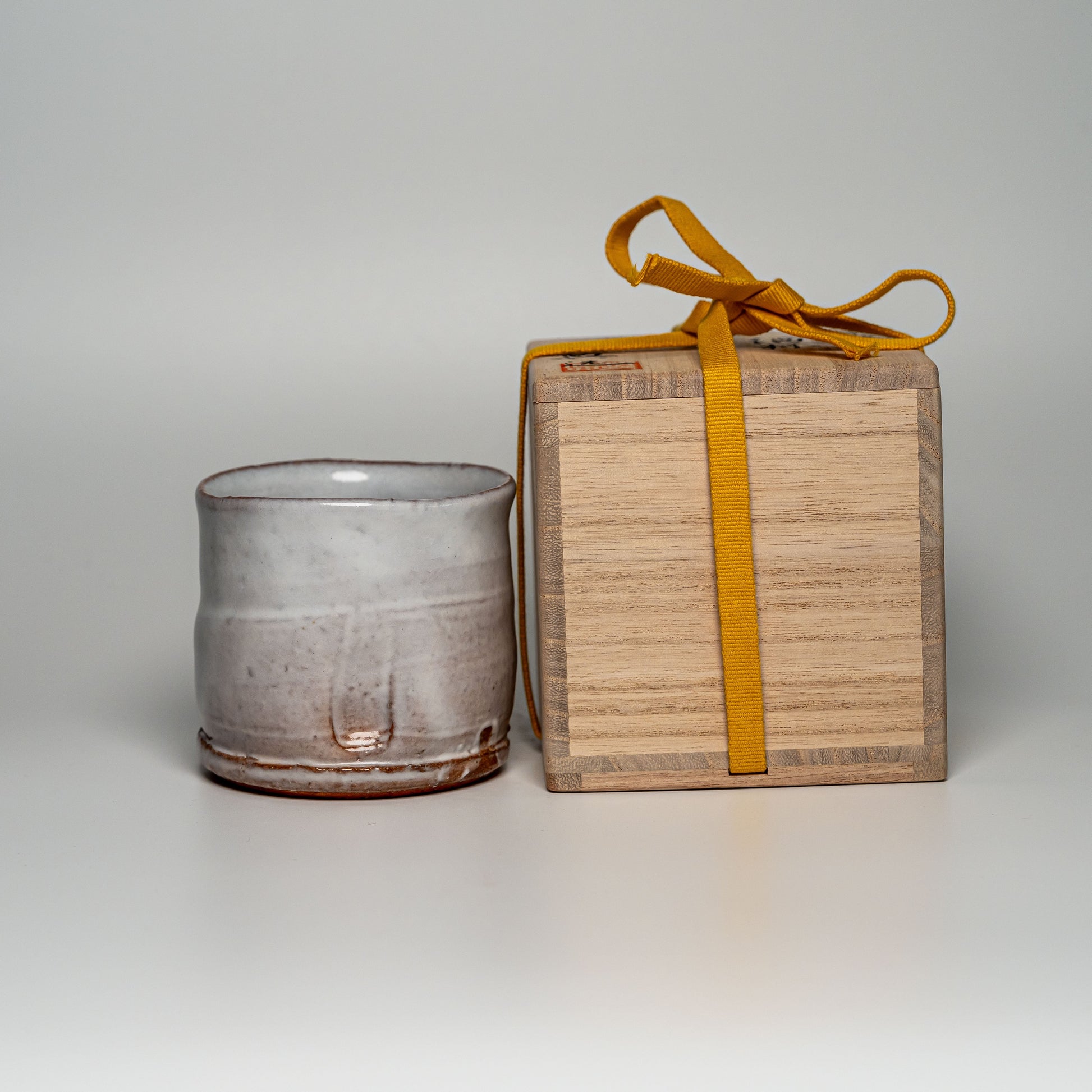 A white Hagi yaki shochu cup next to its wooden box on a white background